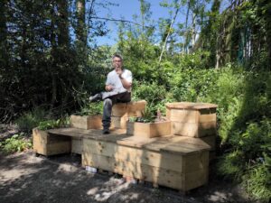 Image shows Chris, a member of Touch Wood staff standing behind one of the reclaimed wood benches created by us for Fairfield Hospital